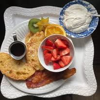A white plate topped with french toast , bacon , strawberries and whipped cream.