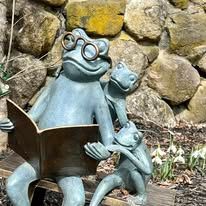 A statue of a frog reading a book to two frogs.