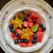 A bowl of watermelon , blueberries and star fruit on a plate.