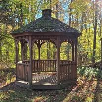 A wooden gazebo is sitting in the middle of a forest.