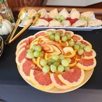 A plate of fresh-cut fruit on a table with tongs and scones in the background.