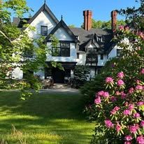 A large white house with pink flowers in front of it surrounded by trees and bushes.