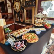 A buffet table with a variety of food displayed on tiers with vintage furnishings and a mirror wall in the background.