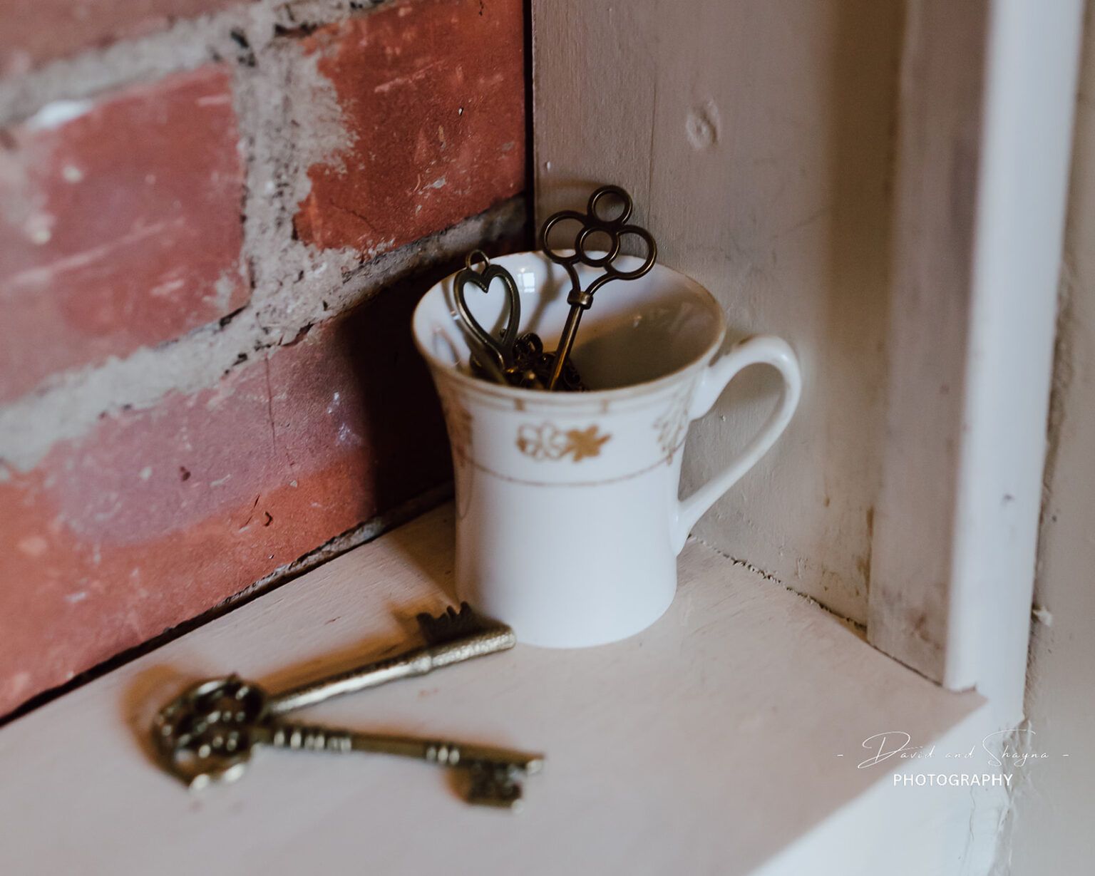 Two keys are in a cup on a shelf next to a brick wall.