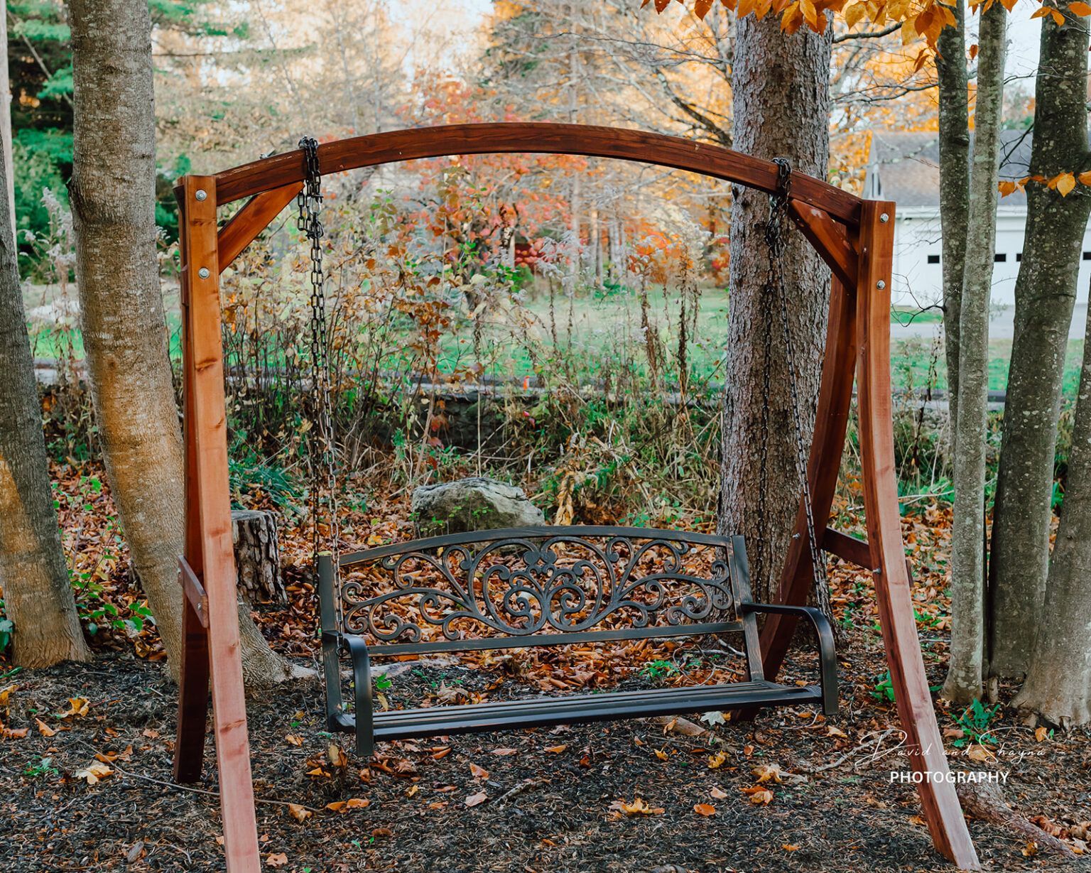 A wooden swing is sitting in the middle of a forest with fall foliage.