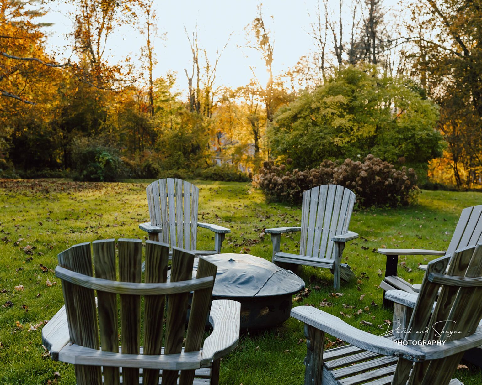 A group of wooden chairs are sitting around a fire pit in the grass.
