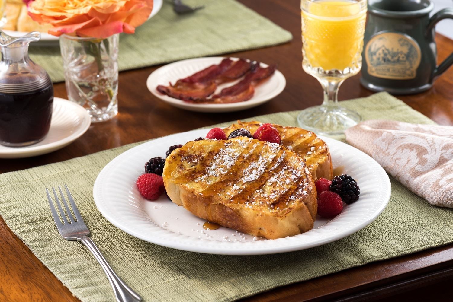A plate of french toast with berries and bacon on a table.