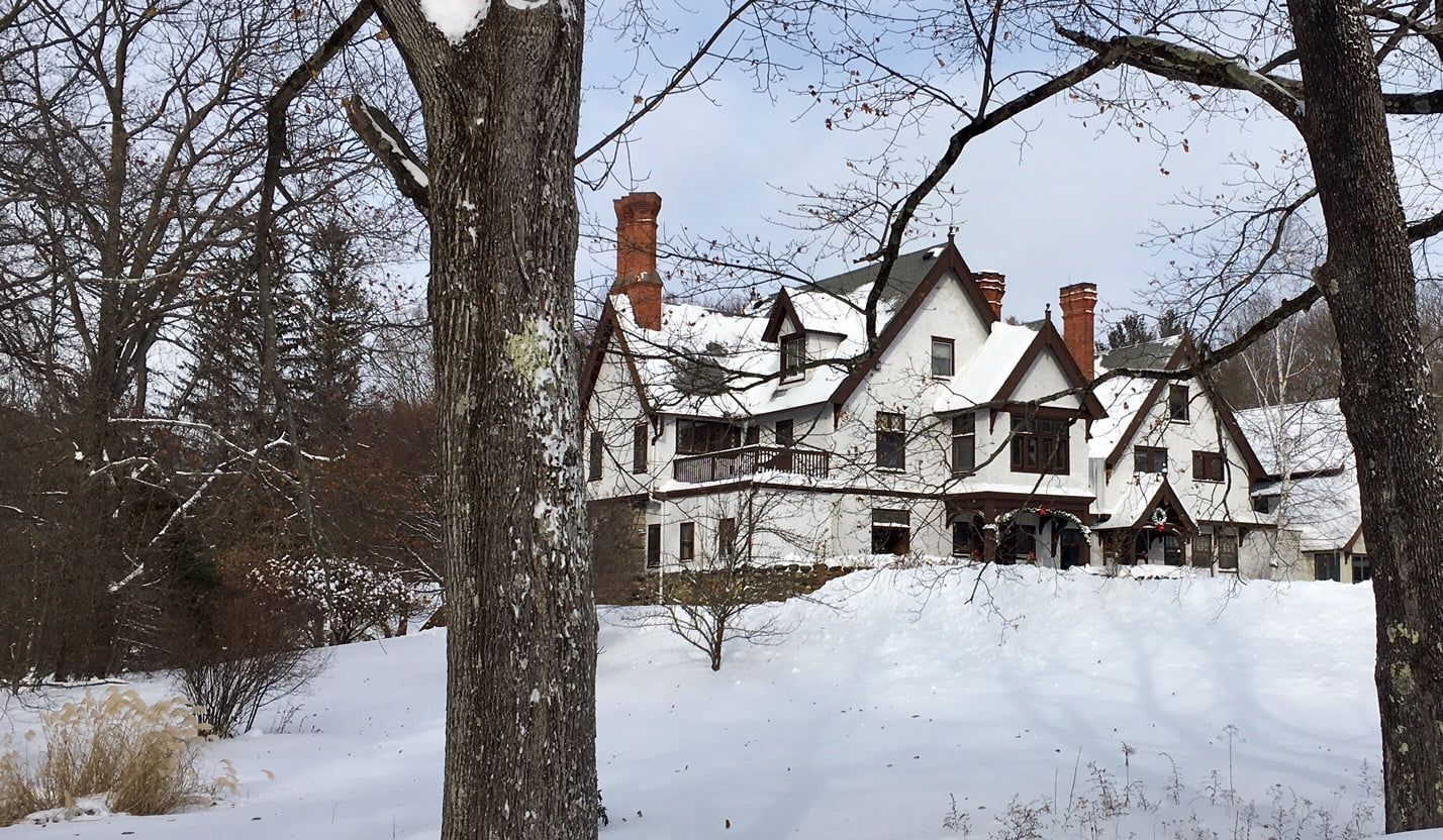 A large white house is surrounded by snow covered trees