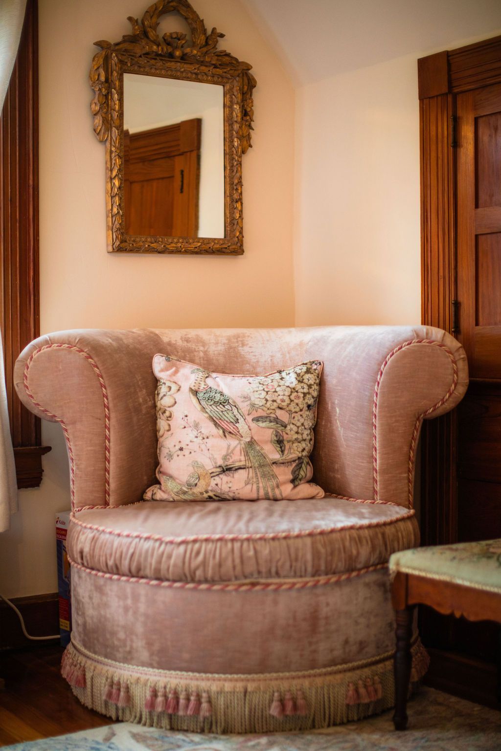 A pink chair with a pillow on it is sitting in a corner of a room next to a mirror.