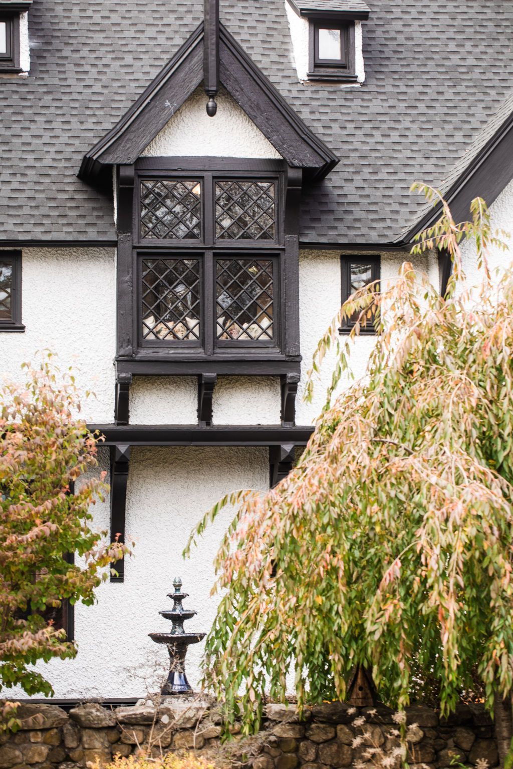A white and black Tudor-style house with diamond-paned windows and a fountain in front of it.