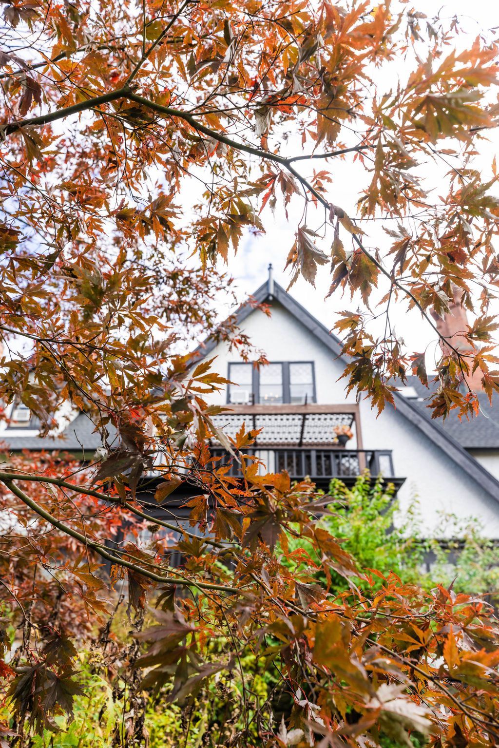 A white house with a balcony is surrounded by trees with autumn leaves.