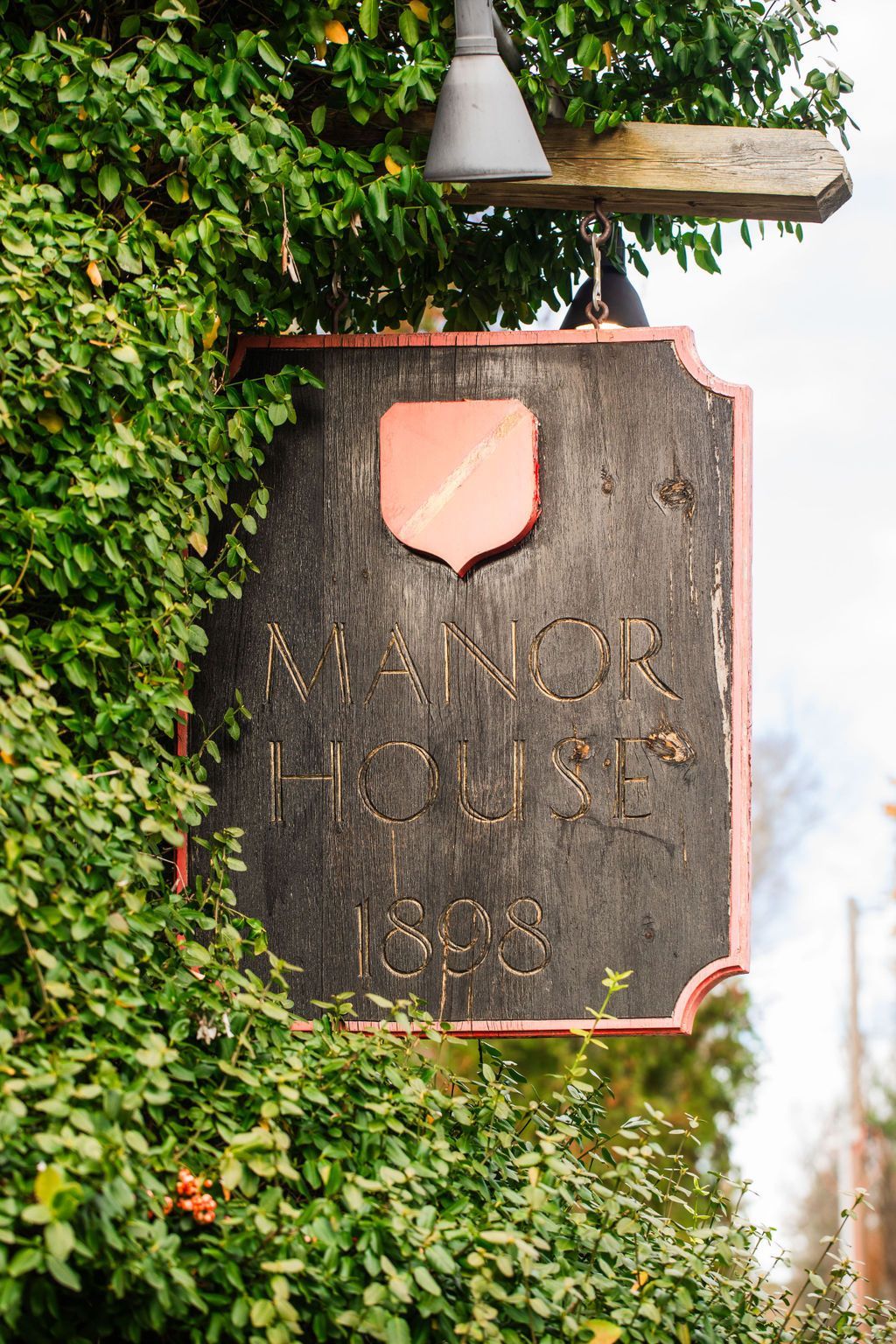 A manor house sign is surrounded by trees and bushes.