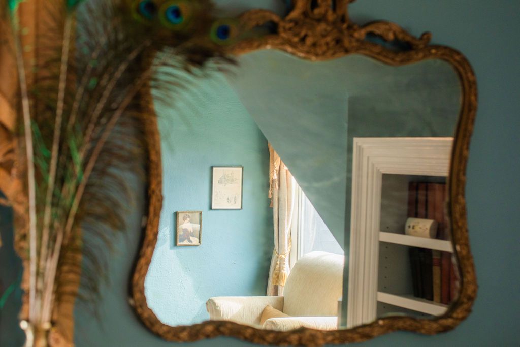 A mirror with a peacock feather on it is hanging on a wall.