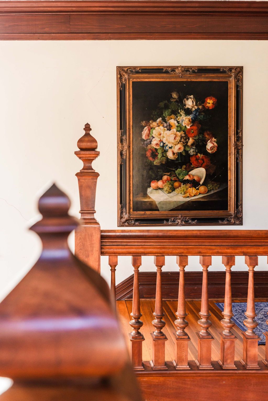 A vintage painting of flowers is hanging on a wall next to an ornate wooden railing.