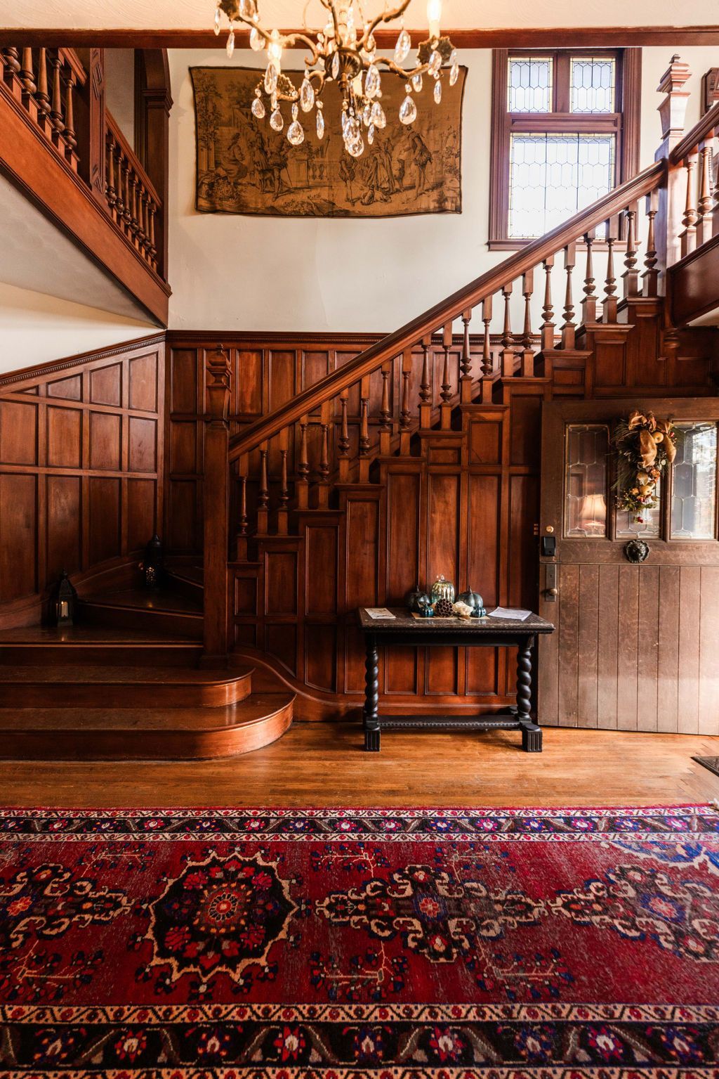 A large wood-paneled staircase in a Tudor-style foyer with a red rug on the floor.