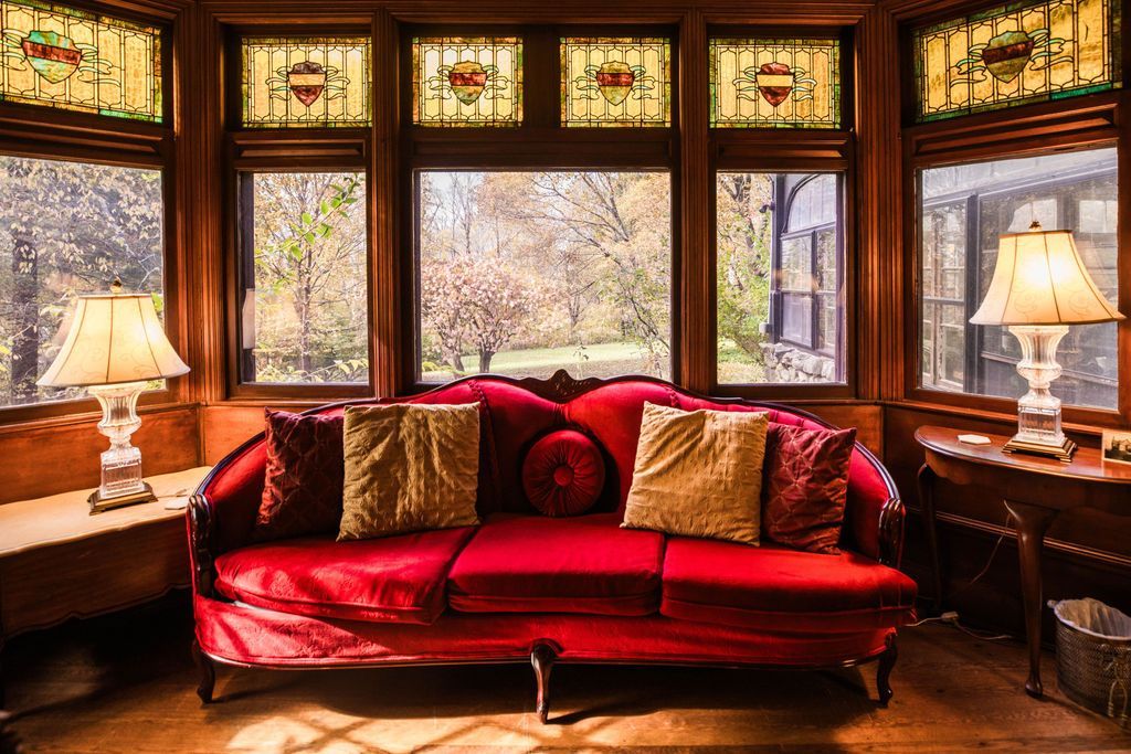 A sitting room with a red velvet couch and stained glass windows and vintage furnishings.
