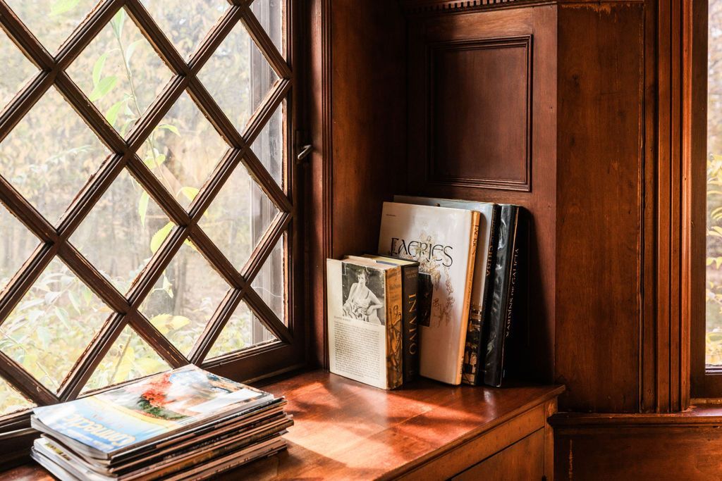 A stack of books sitting on a wooden windowsill next to a diamond-paned window.