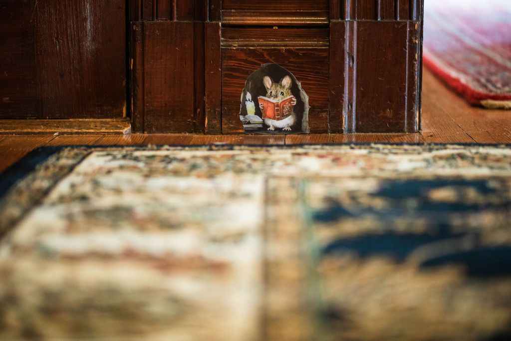 An animated mouse is sticking its head out of a hole in a door.