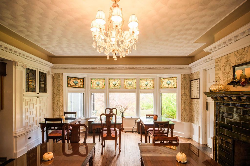A Victorian dining room with tables and chairs, a fireplace, and a chandelier hanging from the ceiling.