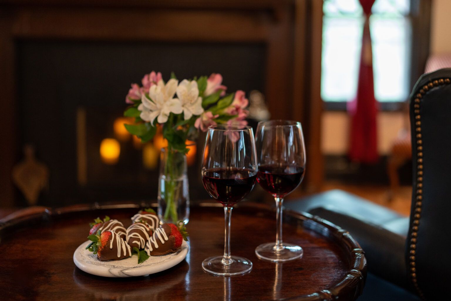 Two glasses of wine and a plate of chocolate covered strawberries on a table.