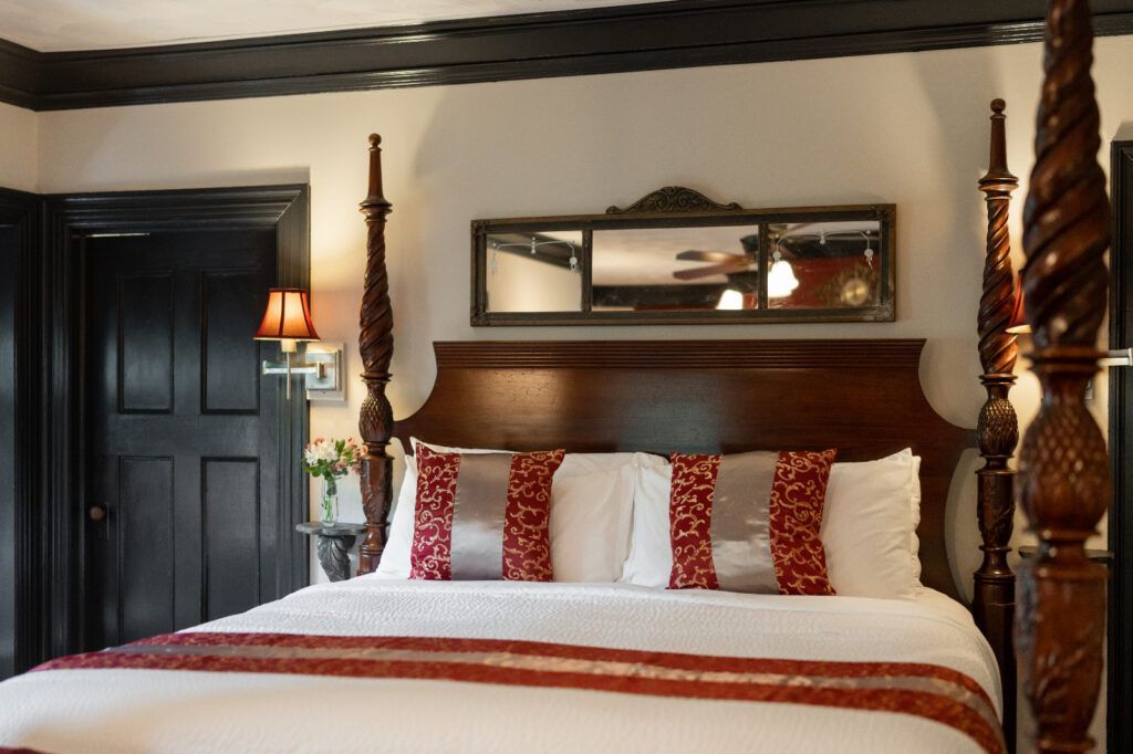 A bedroom at a New England Country Inn with a four-poster bed and a mirror on the wall