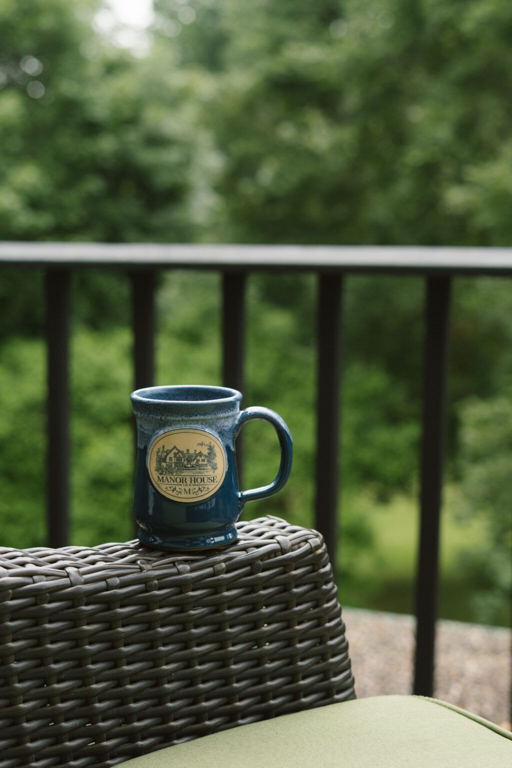 A blue coffee mug is sitting on a wicker chair on a balcony.