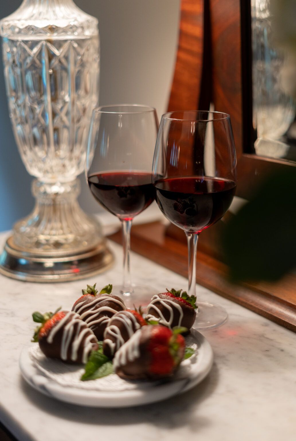 Two glasses of red wine and chocolate covered strawberries on a table.