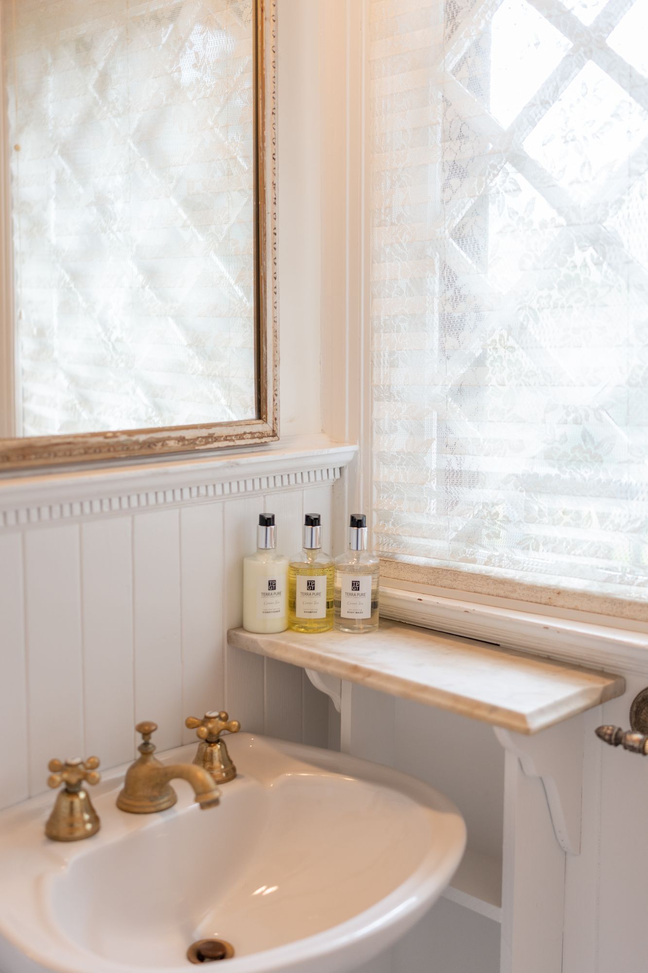 A bathroom with a sink , mirror , shelf and window.