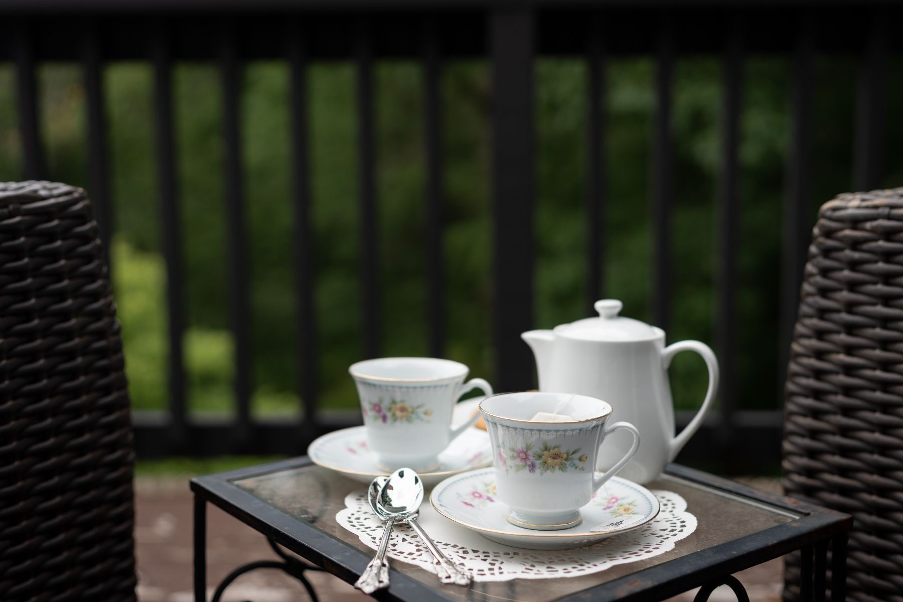 A tea set is sitting on a glass table on a balcony.