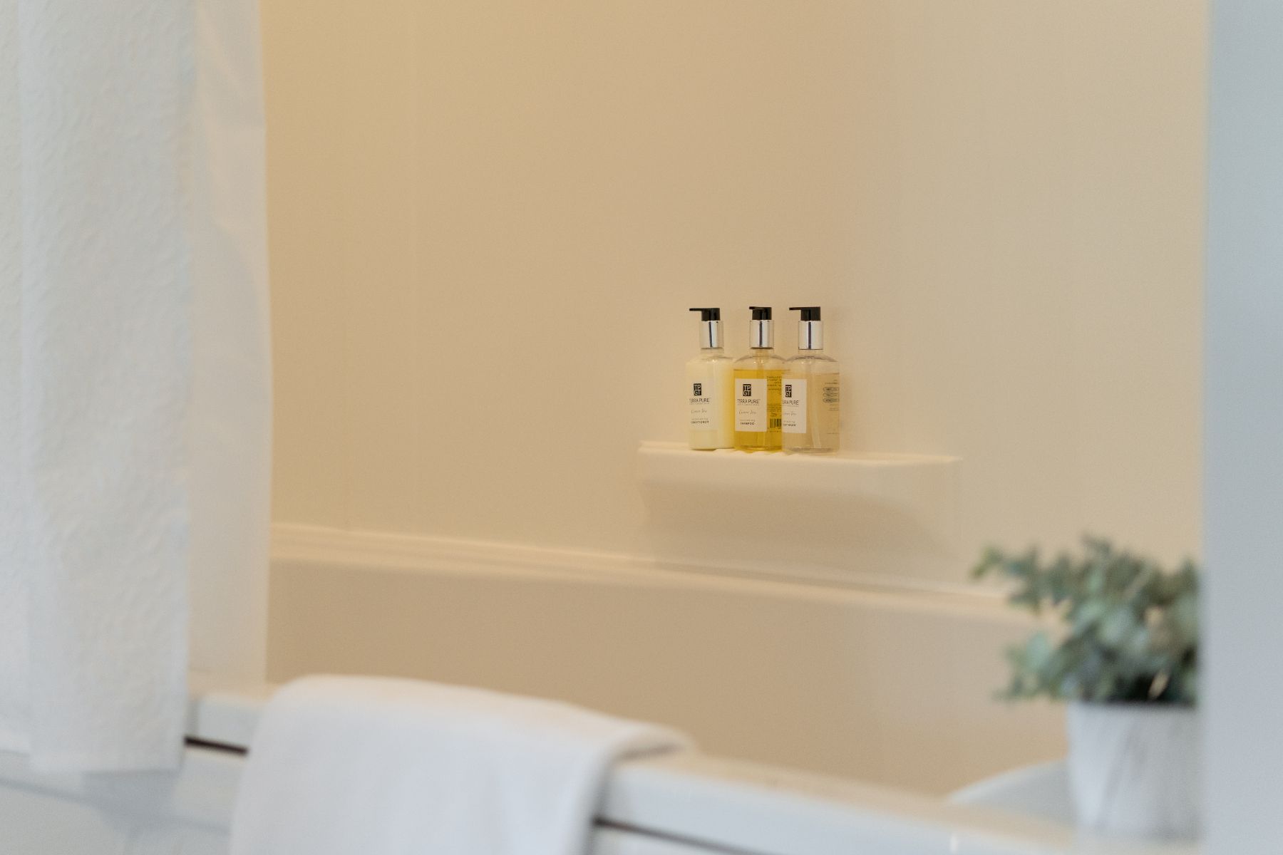 There are three bottles of high-end bathroom toiletries on a shelf next to the bathtub.
