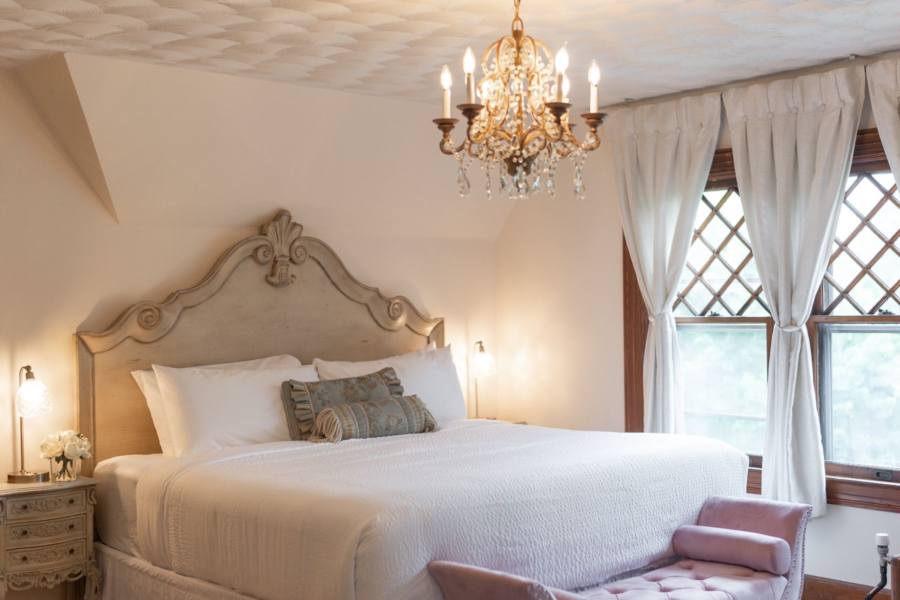 A bedroom styled with country French furnishings at a New England Country Inn with a large bed and a vintage chandelier hanging from the ceiling.