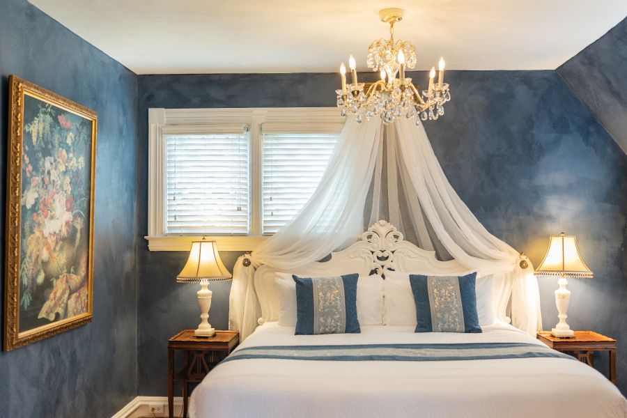 A bedroom at a New England Country Inn with a king-size bed with bedcrown and canopy, lamps, and a chandelier.