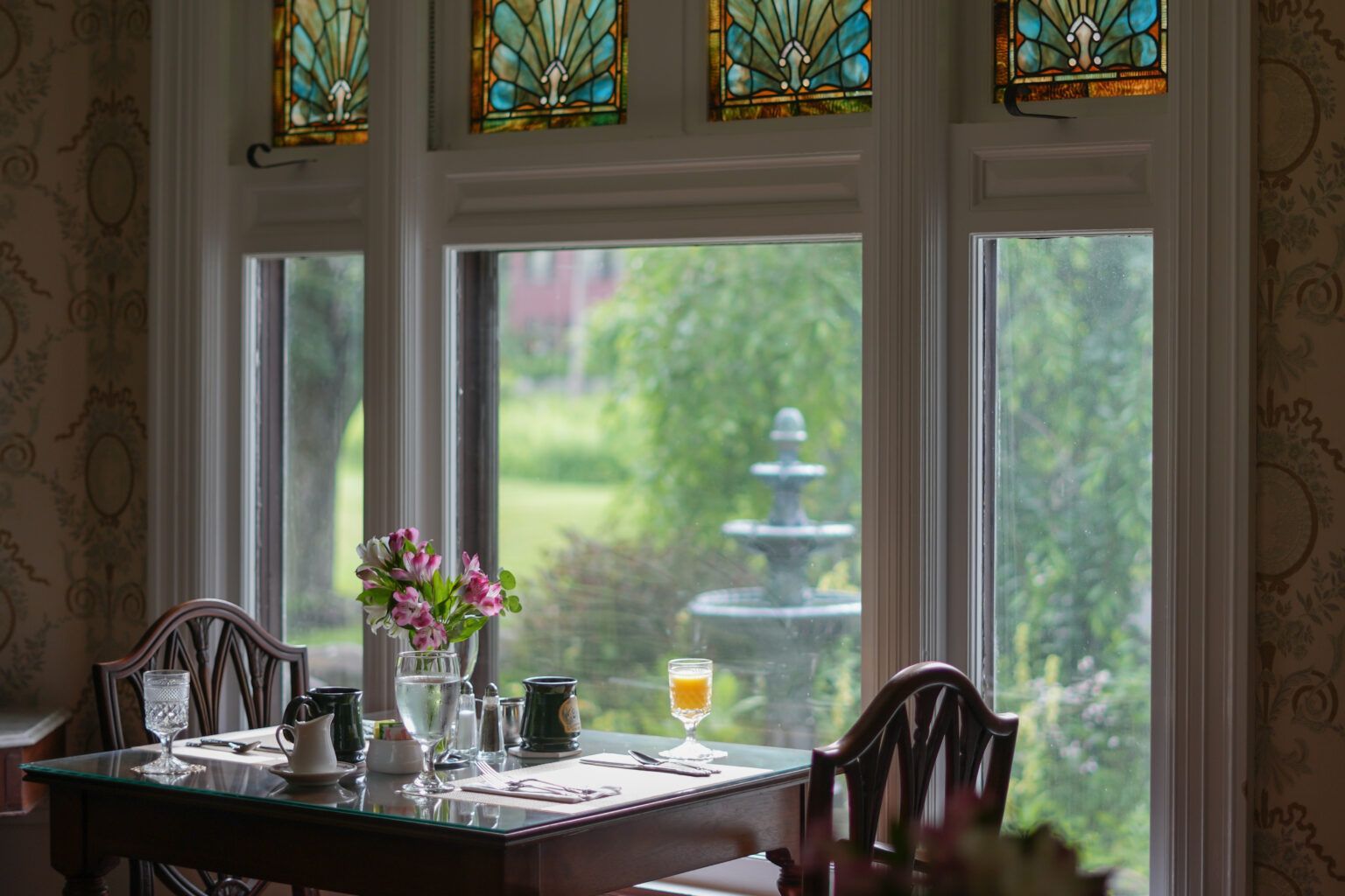 A romantic dining room table with a vase of flowers on it and a fountain in the background.