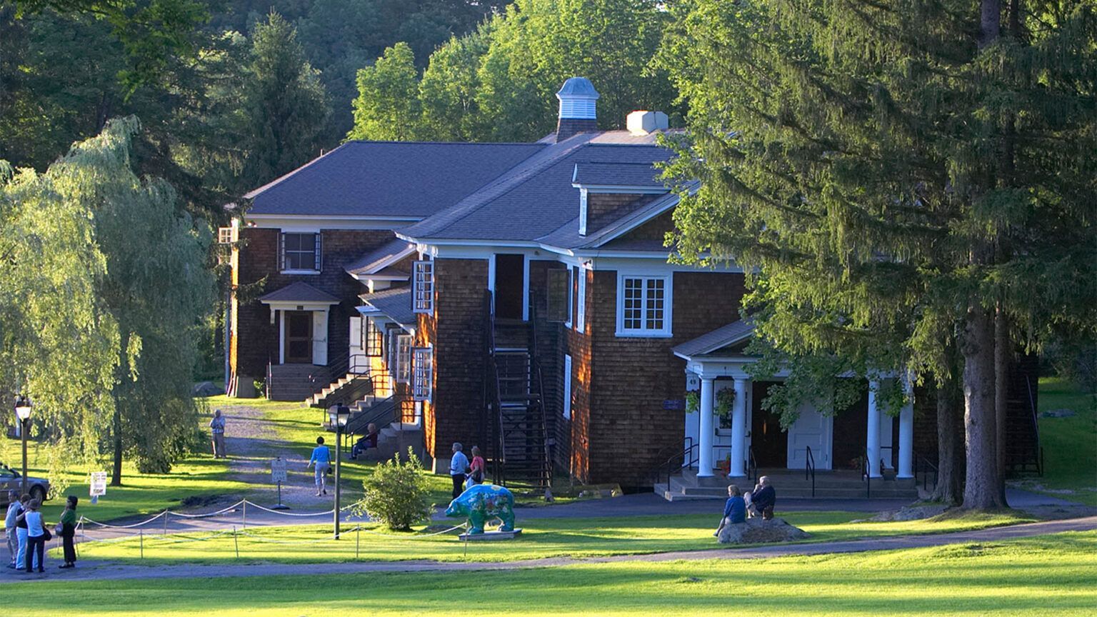 A group of people are standing in front of a large house surrounded by trees.