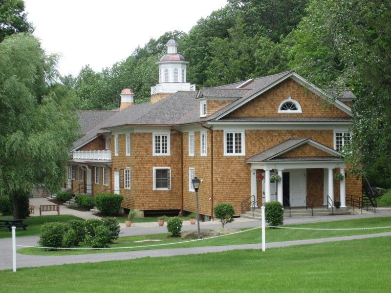 A large brown house with a gray roof is surrounded by trees