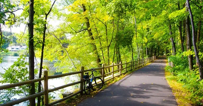 A bicycle is parked on the side of a path next to a river.