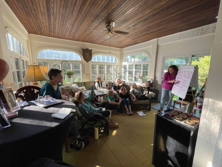 Group of people in a sunroom, attending a workshop. Woman presents at a whiteboard.