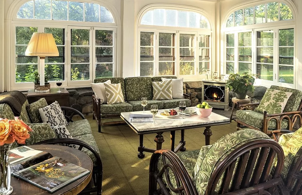 Sunroom with green floral furniture, stone fireplace, and arched windows.