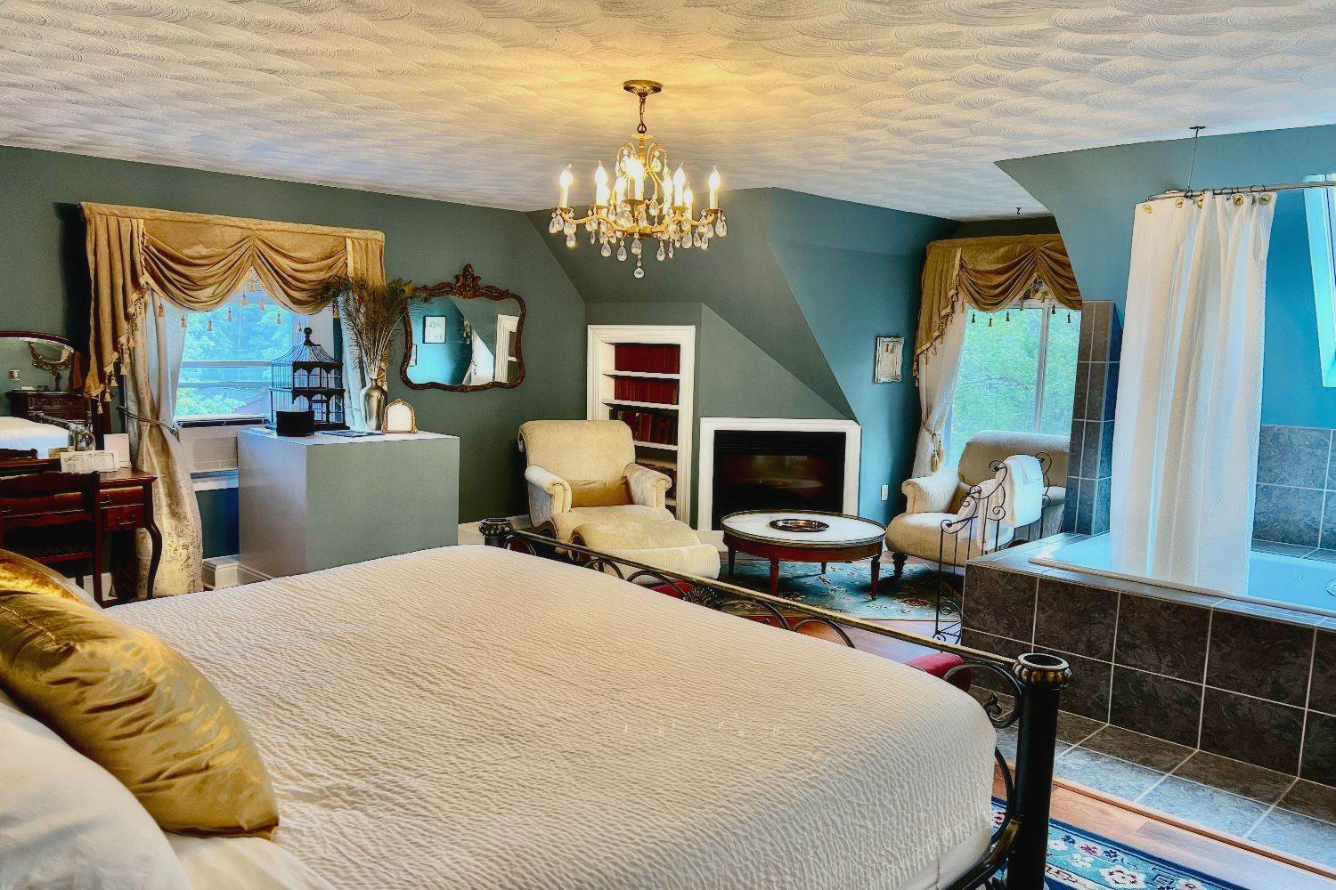 A Victorian bedroom at a New England Country Inn with a king-size bed, chandelier, sitting area,  and oversized soaking tub in the room. 