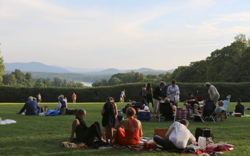 A group of people are having a picnic in a park with mountains in the background.