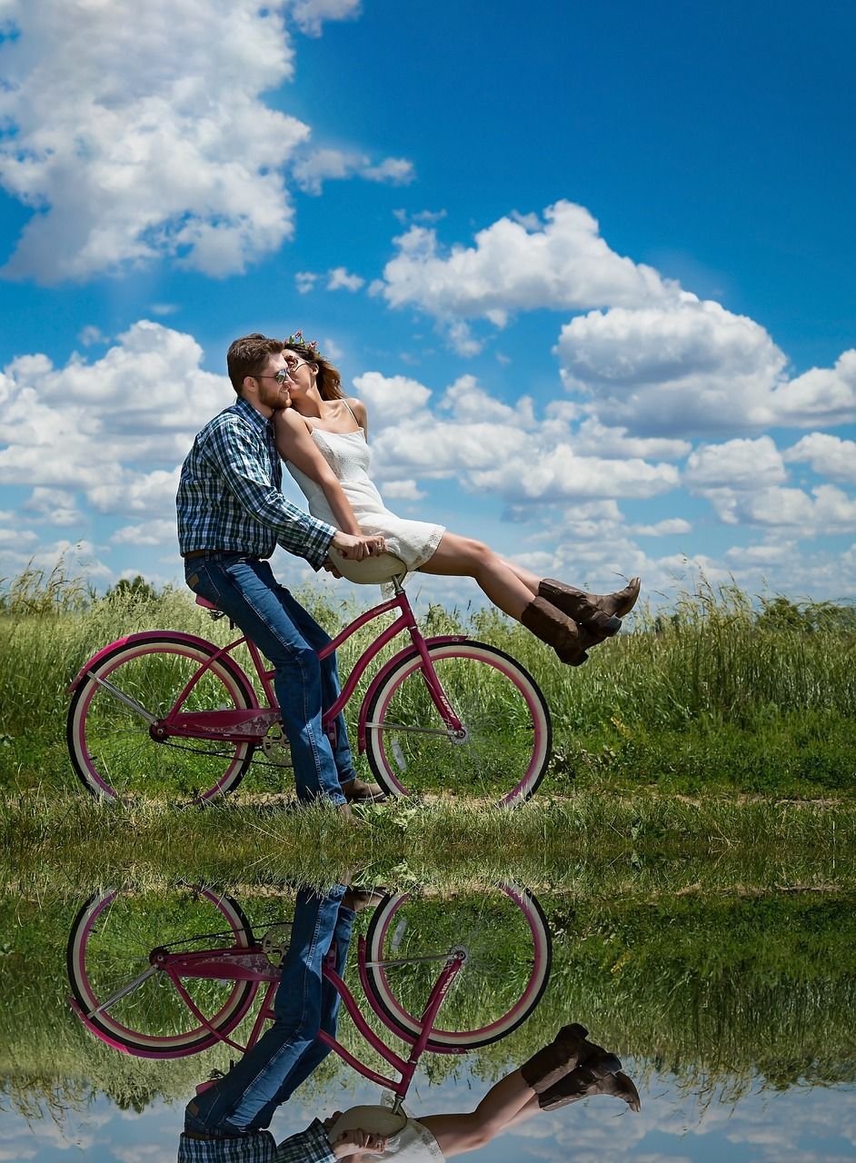 A man is carrying a woman on a bicycle in a field.