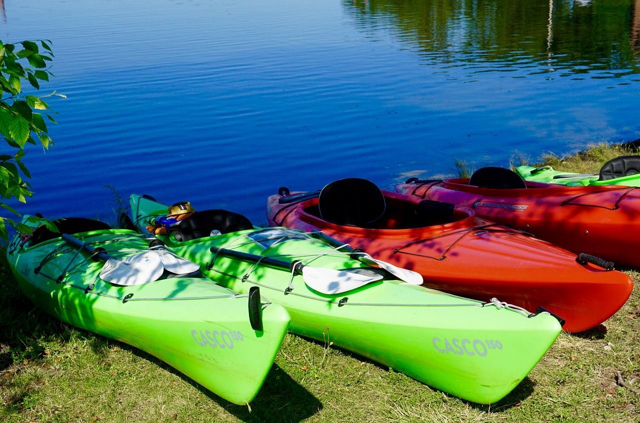 Three green and red kayaks are sitting on the grass near a lake.