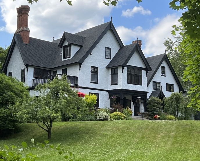 A large white house with a black roof is sitting on top of a grassy hill.