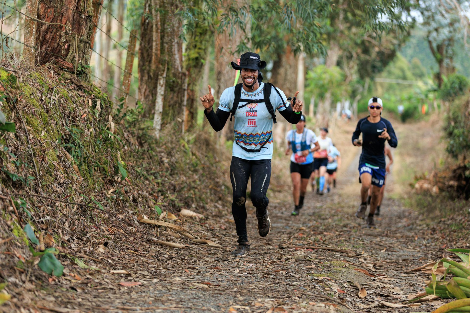 A group of people are running down a dirt path in the woods.