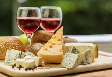A wooden cutting board topped with different types of cheese and two glasses of red wine.