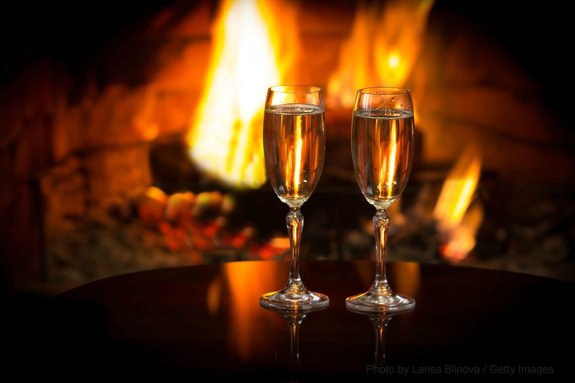 Two glasses of champagne are on a table in front of a fireplace.