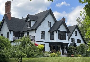 A large white Tudor-style house with a pitch black roof and ornate brick chimneys