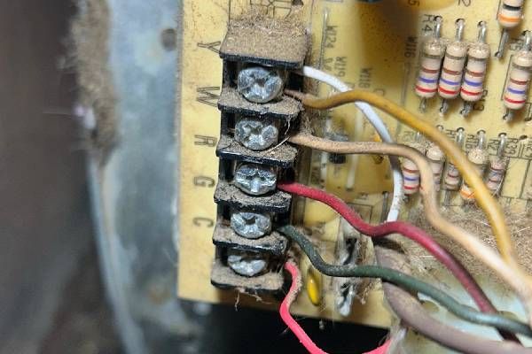 A close-up of a dusty HVAC control board terminal block with five colorful wires connected to Y, W, R, G, and C ports.