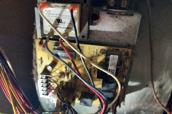 A circuit board with wires and a mounted transformer inside a dusty furnace control panel.