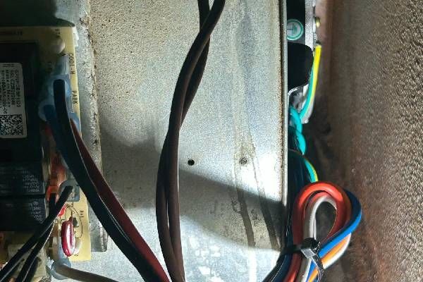 Close-up of electrical wiring connected to a circuit board inside a metal appliance housing.